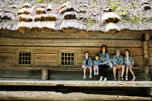 Family of five posing by a rustic wooden house with traditional thatched roof, a Person Photo by AS photostudio