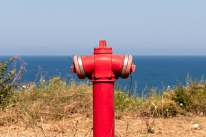 Bright red fire hydrant standing against a clear blue sky and calm ocean, surro, a Technology Photo by Ales Munt