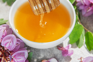 Natural honey dripping from dipper into bowl with acacia flowers, a Food & Drink Photo by Olena Rudo