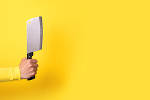 Close-up of a hand gripping a meat cleaver against a bright yell, a Food & Drink Photo by Ales Munt
