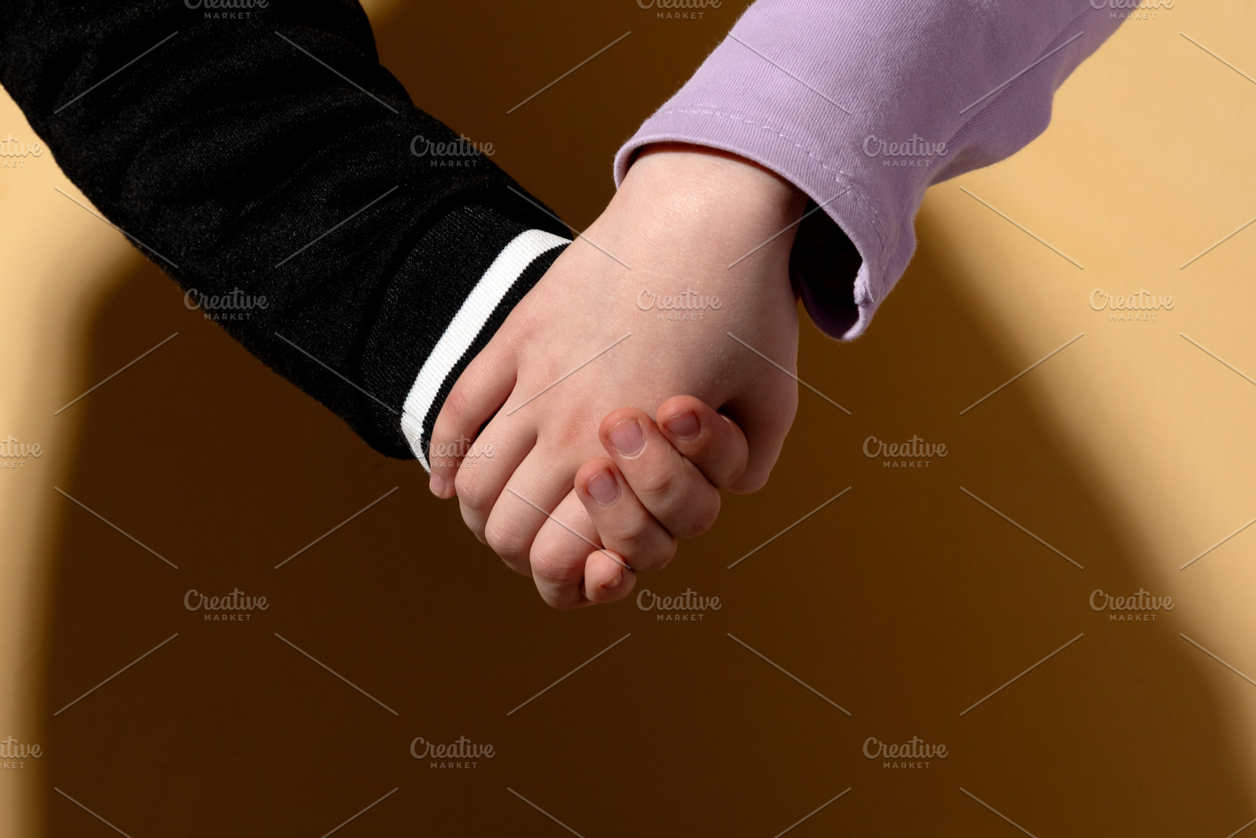 Closeup of two children holding hands on a beige background, sym, a Person Photo by Ales Munt