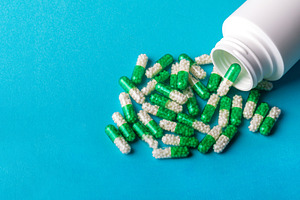White plastic bottle with green and white capsules spilled on blue background,, a Health & Medical Photo by Ales Munt