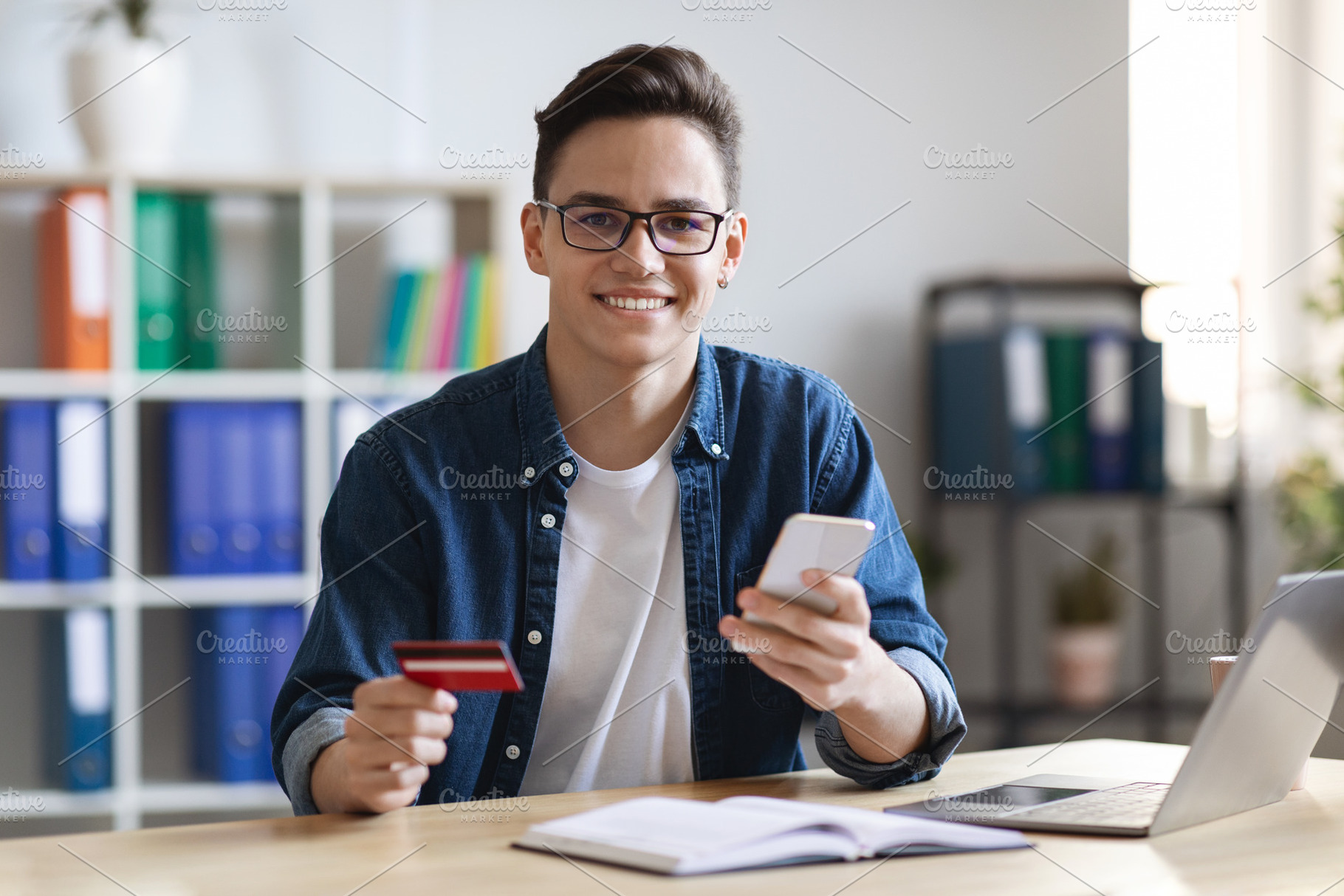 Young Man With Smartphone And Credit Card Sitting At Desk In Office, a Photo by Prostock-Studio