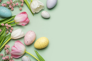Easter eggs and tulips creating a border on pastel green backgro, a Photo by Olena Rudo