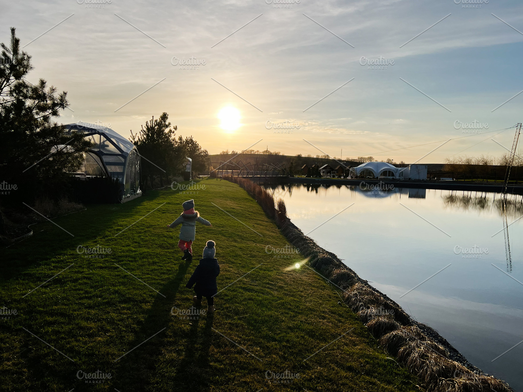 Children playing near a serene lake during sunset amidst nature's beauty, a Photo by AS photostudio