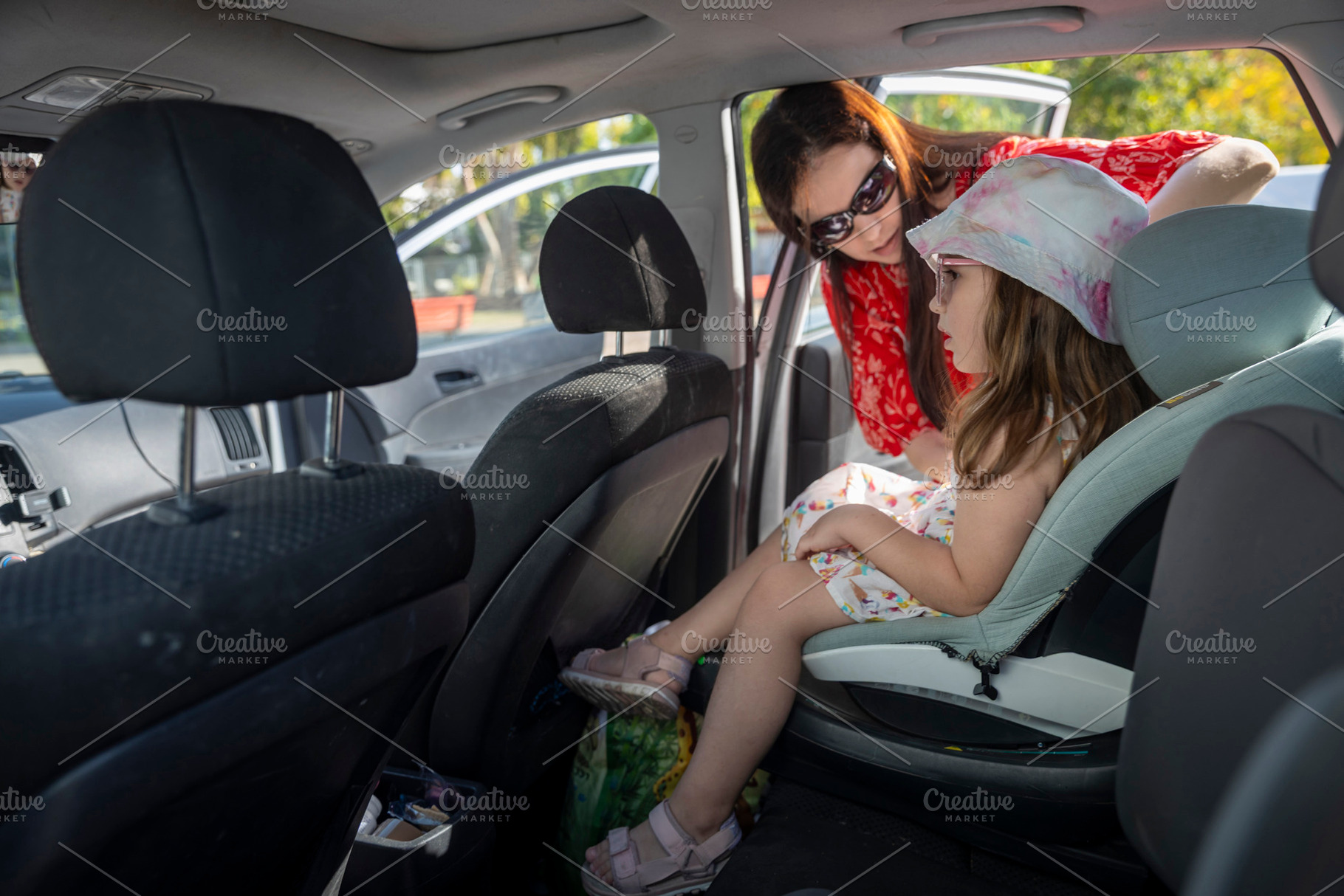 Mother helping her daughter into a car seat in the back of a veh, a Person Photo by Imaginarium