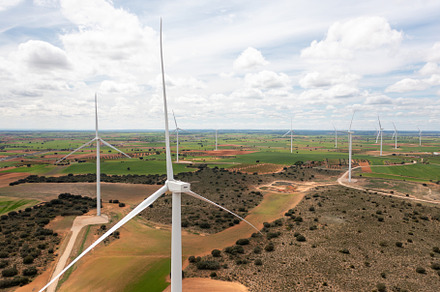 Wind turbine spinning over colorful farmland under bright cloudy sky