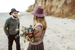 Country style wedding. Newlyweds with rustic bouquet in hands stand on seashore. Outdoors. Artwork