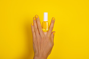 Female hand with yellow polished nails holding a yellow nail pol, a Beauty & Fashion Photo by Ales Munt