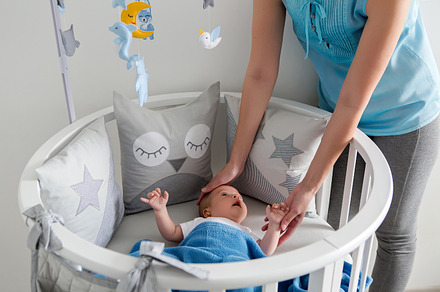 Mother in a blue jacket stands next containing baby, bed, and child, a Person Photo by SaulichPhoto