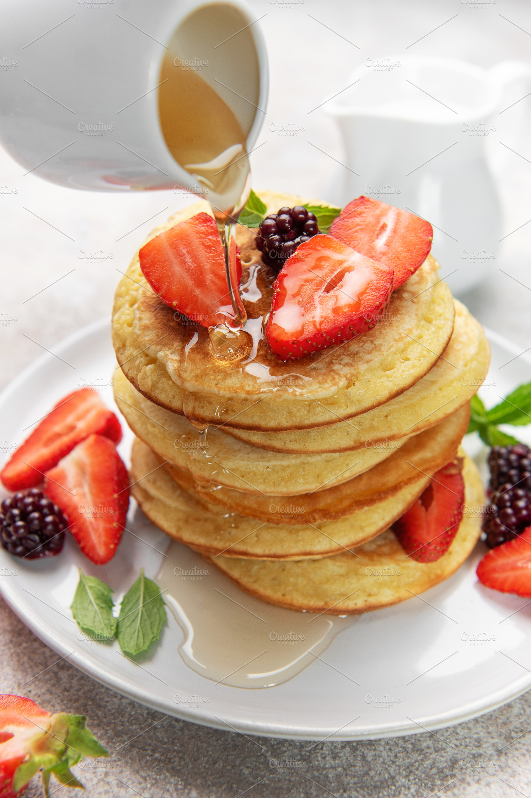 Pouring syrup over homemade pancakes with fresh berries, a Food & Drink Photo by Olena Rudo