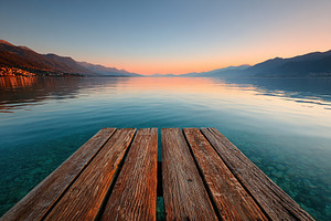 Twilight reflections on a tranquil lakeside dock with serene mountain views, a Photo by AlyaAnd