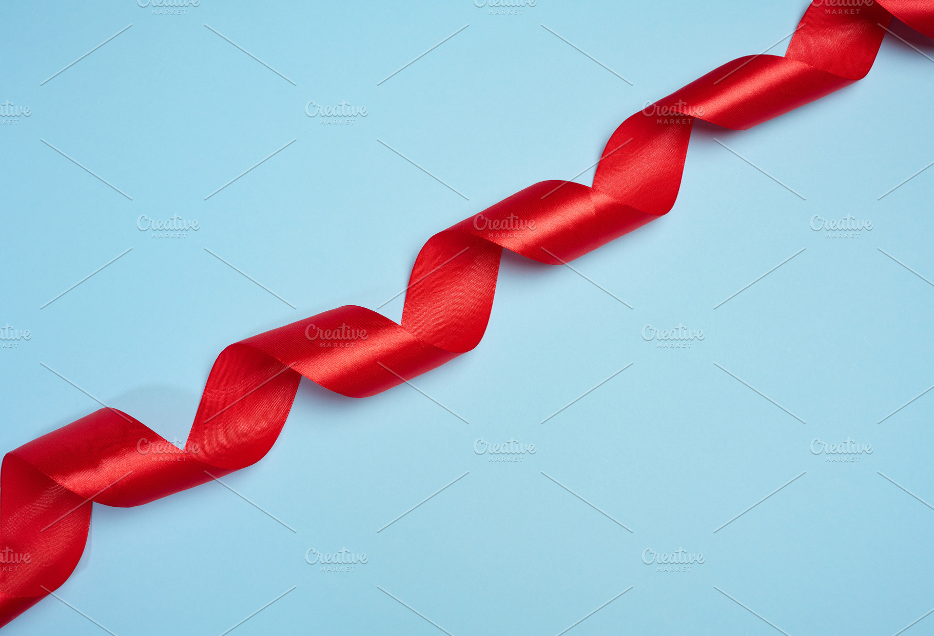 A red satin ribbon twisted into a spiral is placed diagonally on, a Background Photo by ndanko