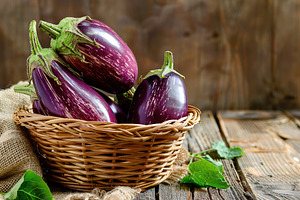 Fresh eggplants in basket on wooden table, a Food & Drink Photo by AlyaAnd
