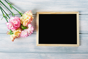 Close up of pink and yellow flowers next to blackboard on wooden table. Copyspace Mockup.