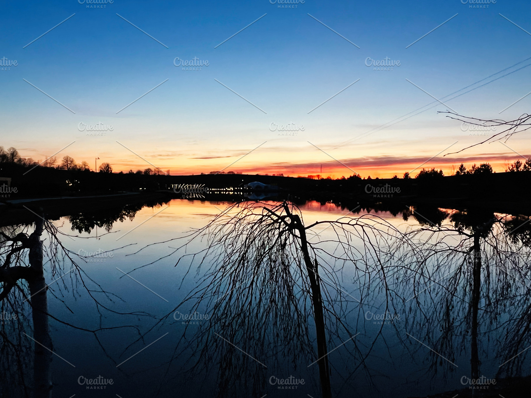 Serene twilight pond reflecting vibrant sunset colors with silhouettes of trees, a Photo by AS photostudio