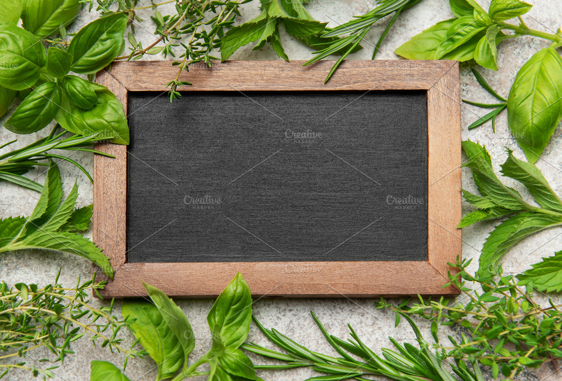 Fresh herbs framing empty chalkboard on gray stone background, a Food & Drink Photo by Olena Rudo