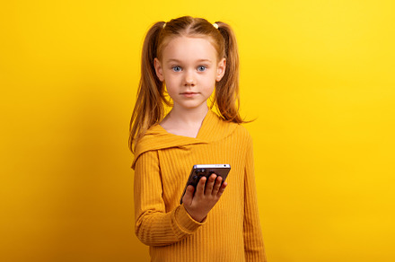 Young girl in a mustard sweater holding a smartphone and looking