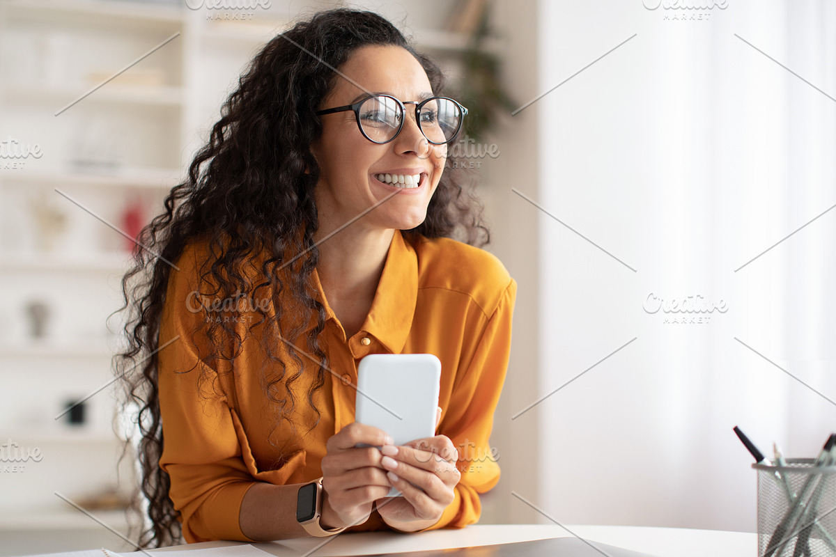 Smiling Arabic Lady Using Smartphone Looking Aside Sitting At Workplace, a Photo by Prostock-Studio (Photo 3 of 4)