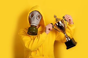 Person in yellow hoodie and gas mask holding a gold trophy on ye, a Person Photo by Ales Munt