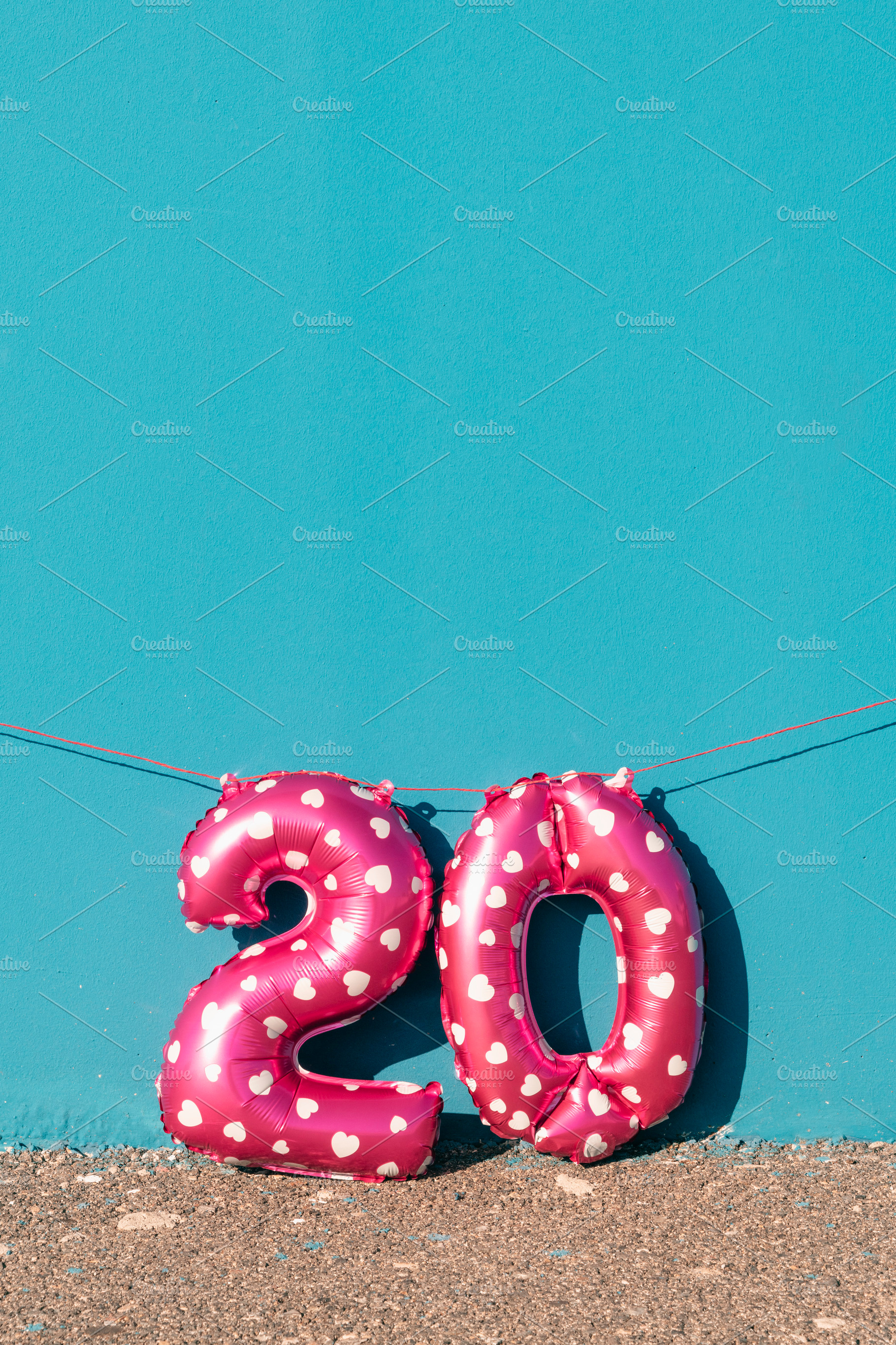 pink number 20 balloons against a vivid blue wall, a Photo by Nito