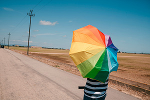man carrying a rainbow umbrella on his shoulders, a Photo by Nito