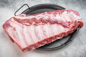 Raw pork spareribs rack in metal tray with rosemary thyme and ga