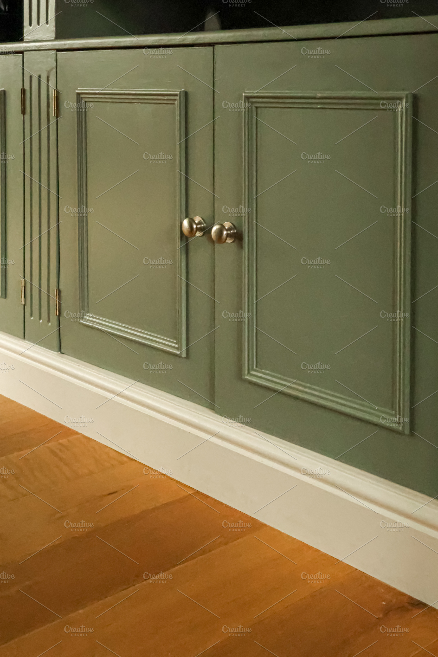 Green wooden cabinet with panel doors and brass knobs, white baseboard accentin, a Photo by Studio ANNA