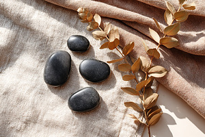 Decorative black stones arranged on fabric with dried leaves during natural lig, a Beauty & Fashion Photo by AlyaAnd