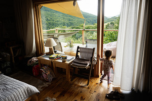 Child exploring beautiful cozy interiors with nature views from a wooden cabin, a Photo by AS photostudio