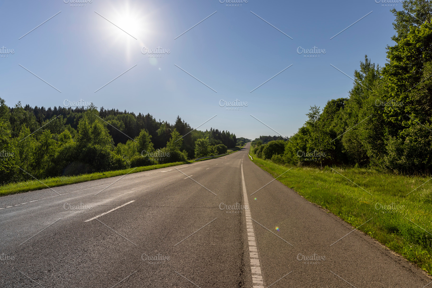 an empty straight paved road against a blue sky background, a Photo by rsoollAI