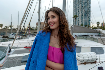 Beautiful woman in pink dress and blue jacket posing on a sailboat in a city ha