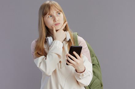 pensive trendy school girl in beige tracksuit using phone, a Person Photo by Alliance Images