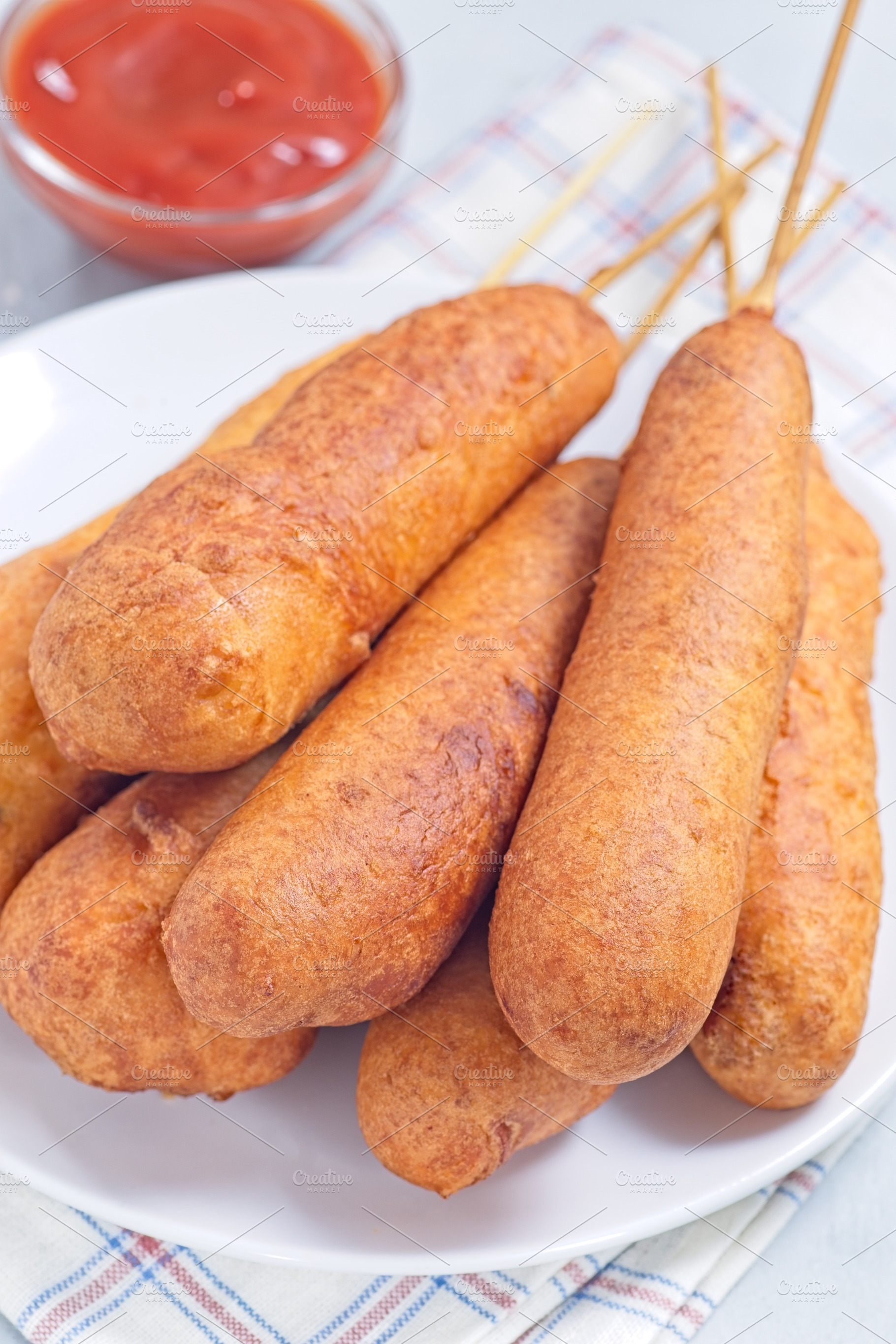 Stack of corn dogs on white plate, served with ketchup, vertical closeup, a Food & Drink Photo by iuliia_n