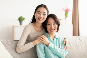 Happy mature Asian woman and her adult daughter hugging and smiling at camera,, a Photo by Prostock-Studio
