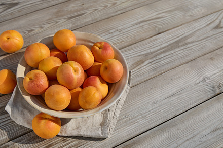 Ripe apricots in bowl on wooden table background in sunlight