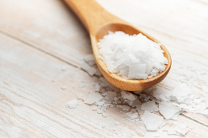 Wooden spoon holding magnesium chloride flakes on white table, a Health & Medical Photo by Olena Rudo