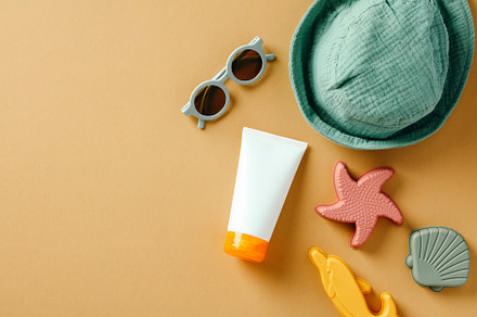 Kids summer accessories and sun screen cream tube on sandy background., a Holiday Photo by photoguns