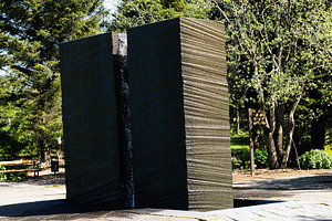Outdoor basalt stone monument in serene park during sunny day with lush trees., a Photo by AS photostudio