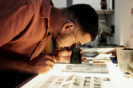 Man, photographer and magnifying glass for film negatives, zoom and analysis for photo journalist job. Photography expert, analyse picture and focus in studio for choice, art decision and creativity, a Photo by Peopleimages.com