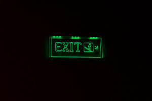 Bright green exit sign glowing in darkness, featuring a running figure and arro, an Architecture Photo by Ales Munt