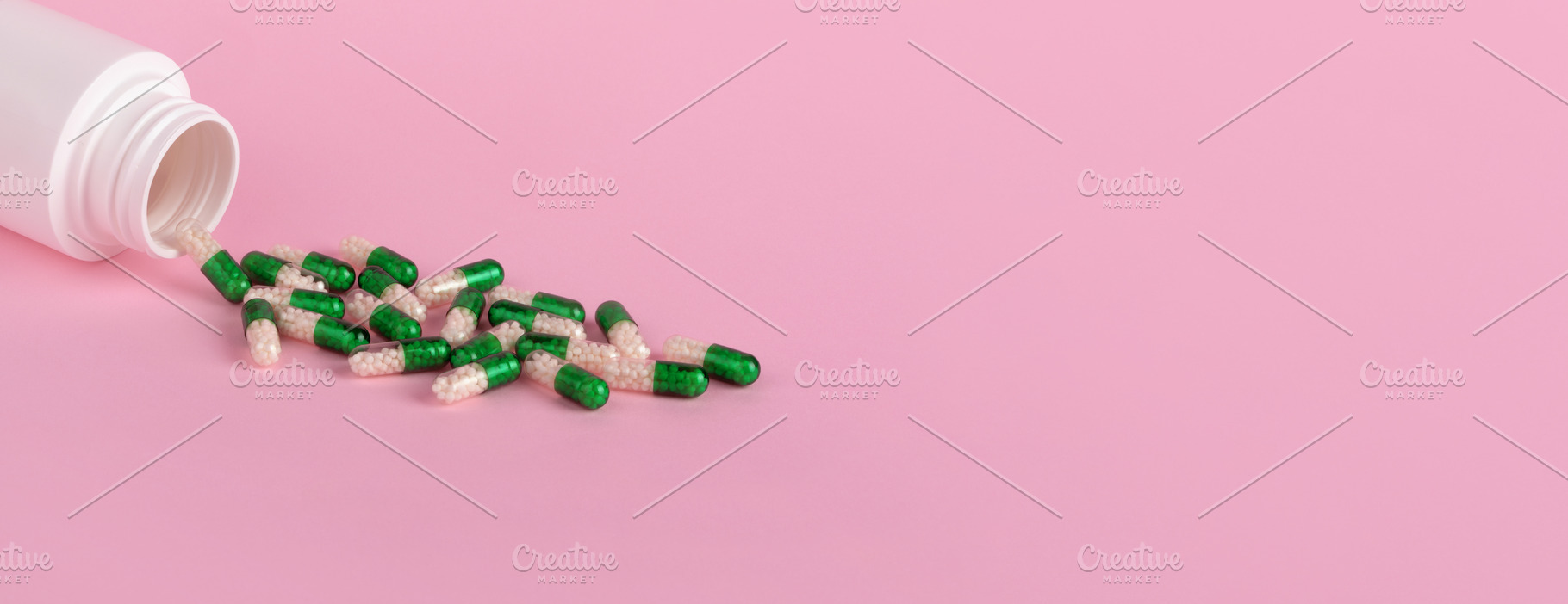 Open white bottle with green and white capsules spilling on past, a Health & Medical Photo by Ales Munt