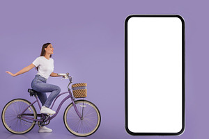 Woman Riding Her Bike Near Huge Smartphone Screen, Purple Background, a Photo by Prostock-Studio