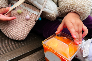 Child holding dessert with caramel topping on a wooden bench outdoors, a Photo by AS photostudio
