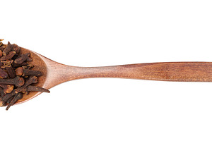 Whole dried clove buds in a dark wooden spoon, isolated on backg, a Food & Drink Photo by ndanko