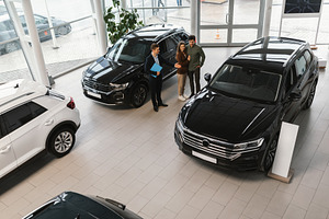 Above view of cheery millennial couple speaking to car salesman about purchasin, a Photo by Prostock-Studio