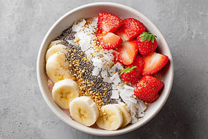 Bowl topped with fresh bananas, strawberries, chia seeds, and coconut flakes fo, a Photo by AlyaAnd