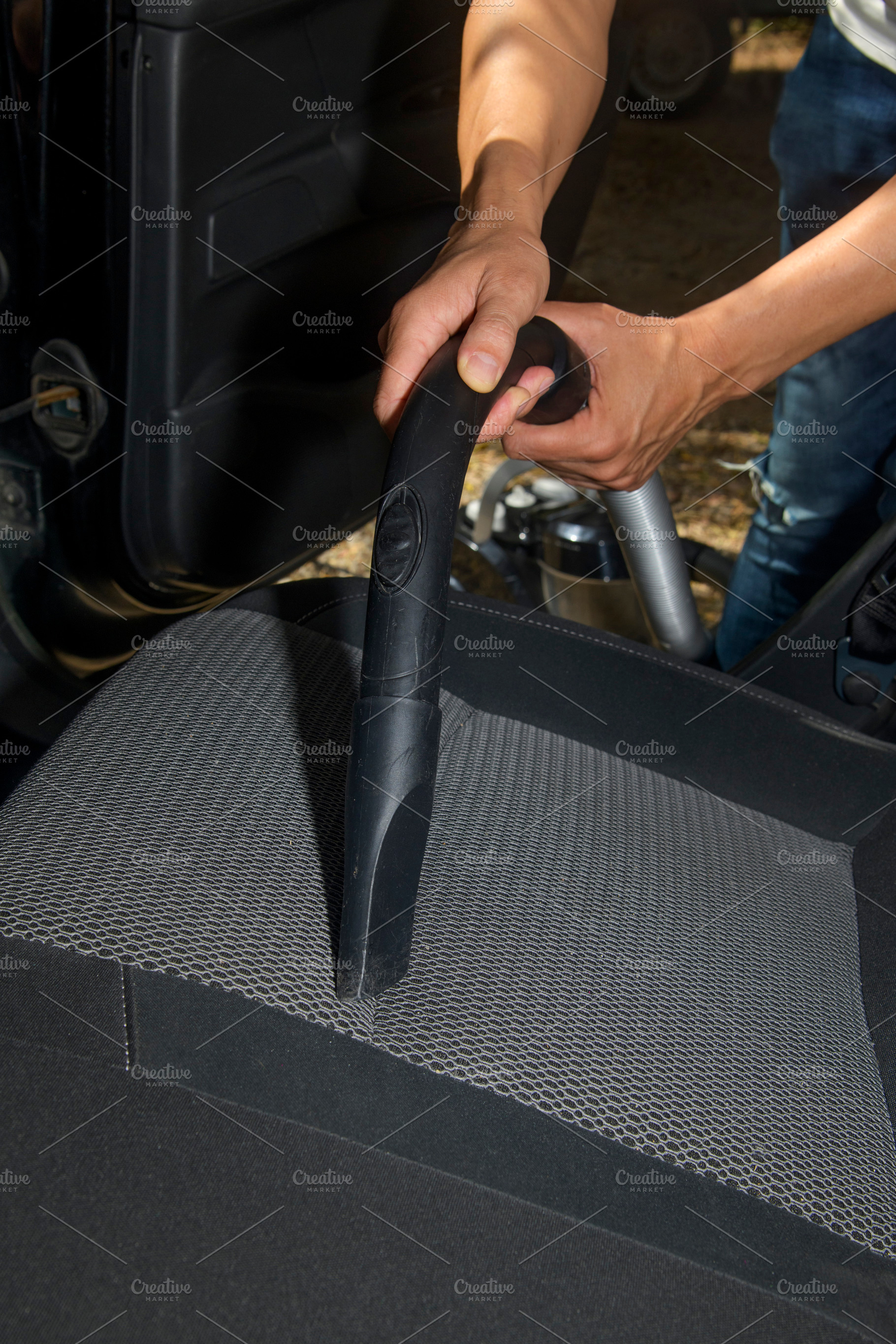 a man vacuuming the seat of a car, a Photo by Nito