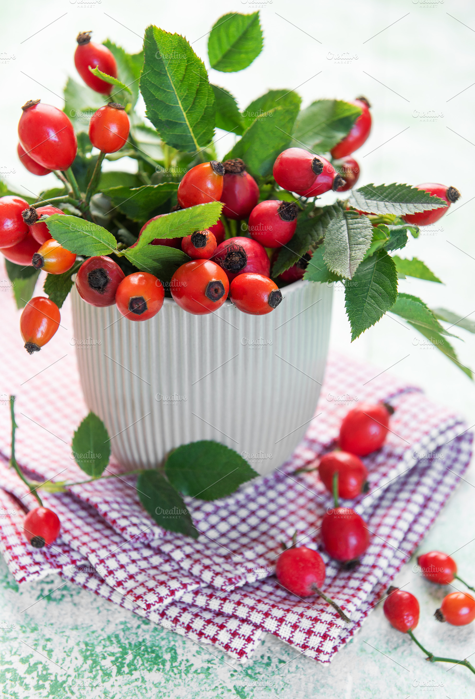 Fresh rose hips with green leaves overflowing a white cup, a Food & Drink Photo by Olena Rudo
