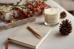Journal with pen, burning candle, and pinecones creating a hygge, a Photo by Studio ANNA